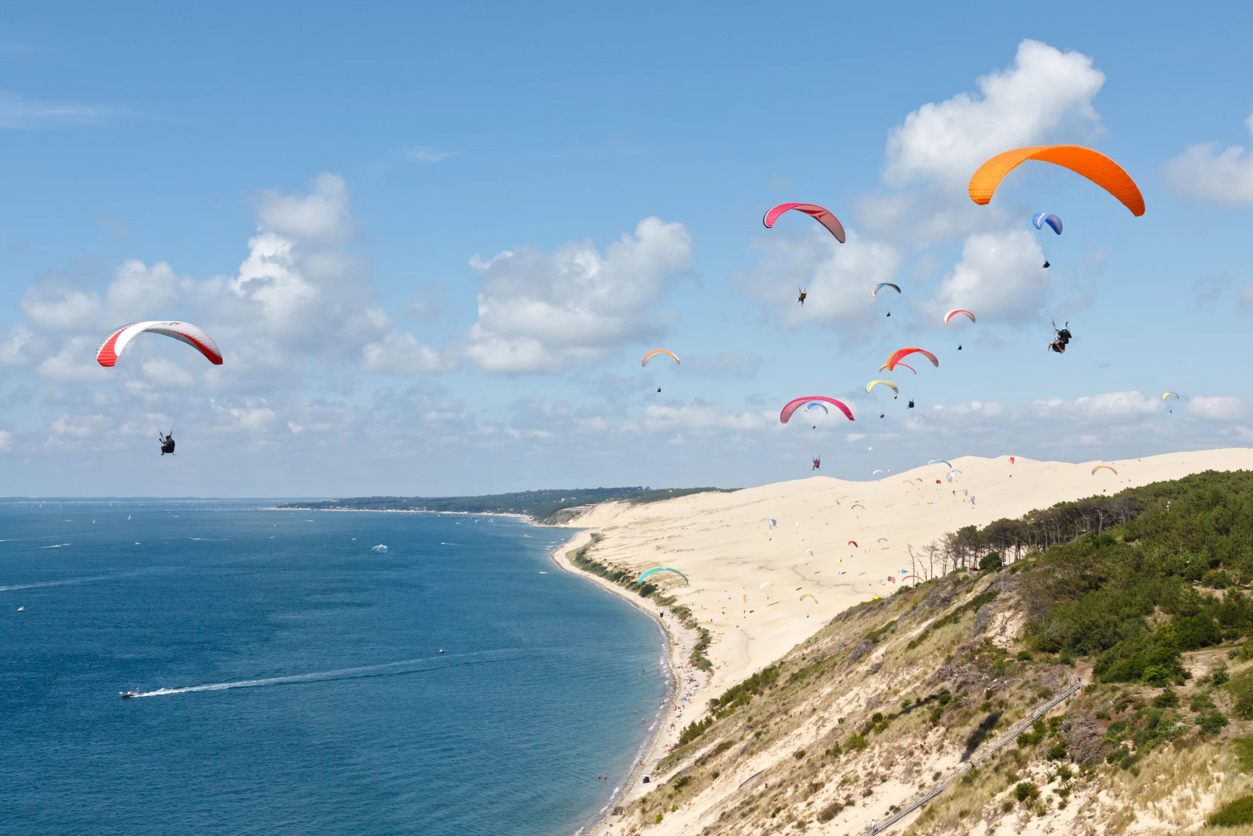 Parapentes survolant la Dune du Pilat, mer en arrière-plan.