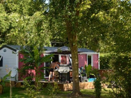 Homme cuisinant barbecue devant mobil-home en forêt.
