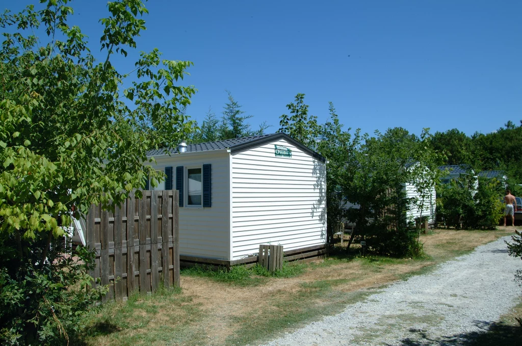 Mobil-home blanc entouré d'arbres au camping.