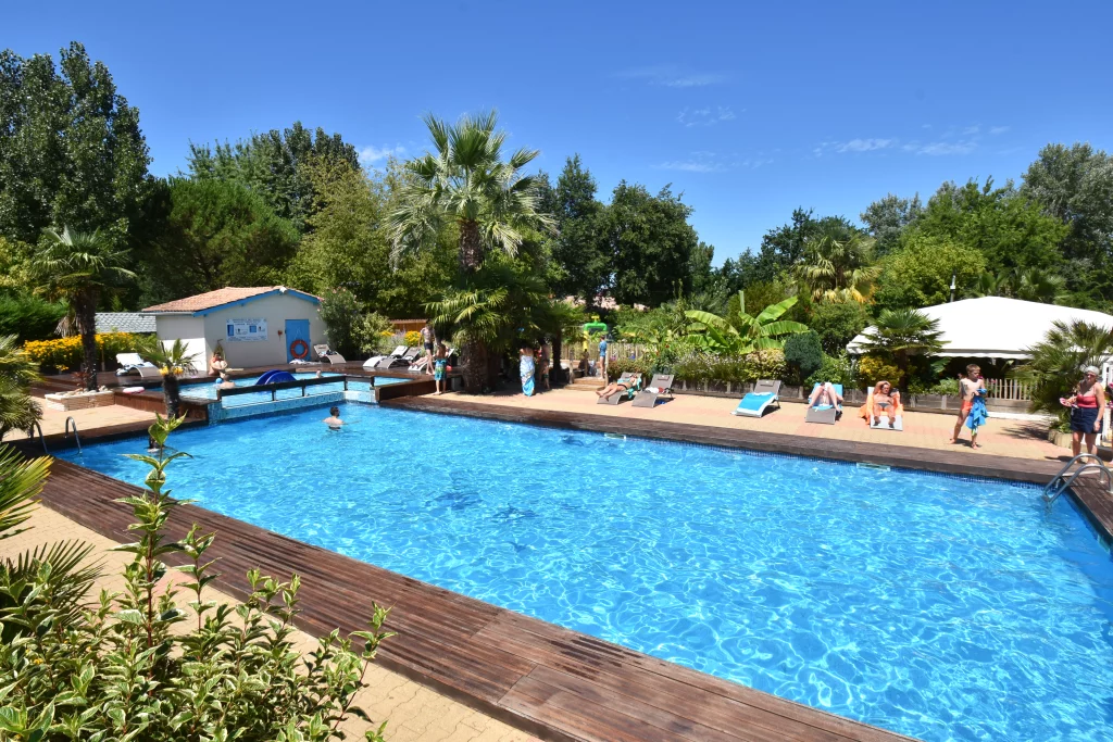 Piscine extérieure entourée de chaises longues et verdure.
