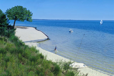 Plage de sable avec mer calme et voilier.