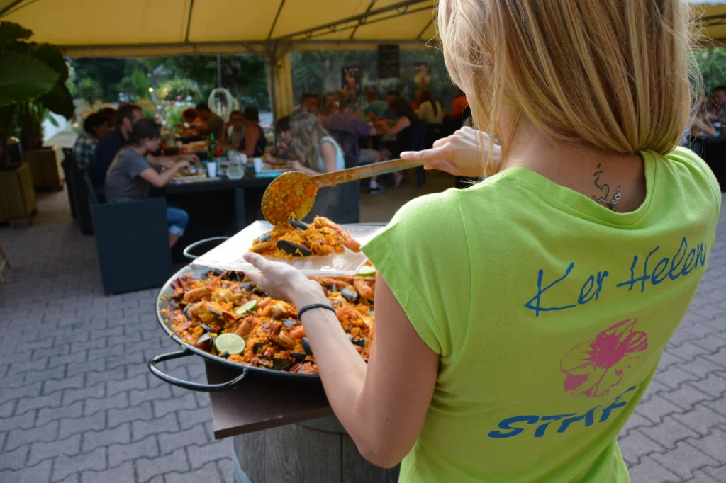 Serveuse proposant paella sous un chapiteau.