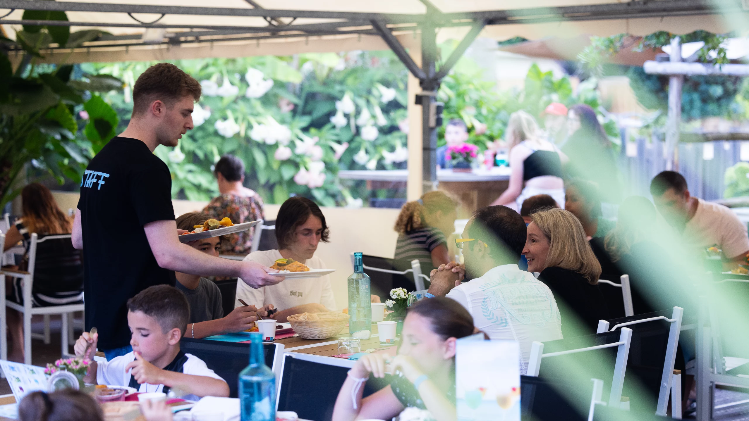 Serveur apportant plats à table en terrasse animée.